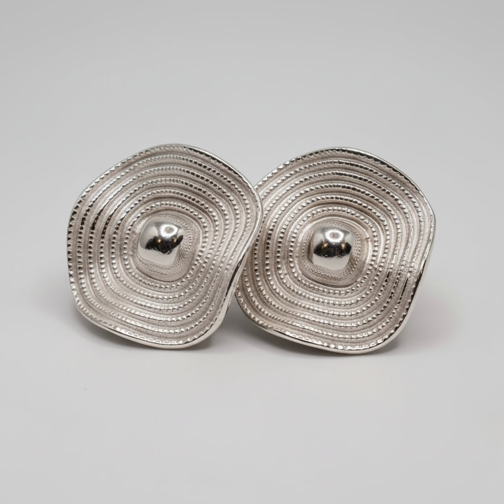 Pair of silver circular earrings on a black cushion against a gray background