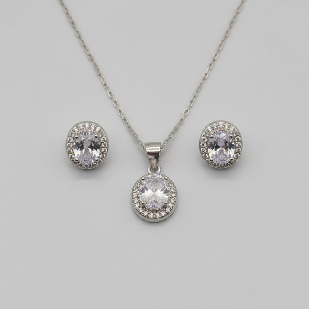 Silver jewelry set with pendant and earrings on a light gray surface.