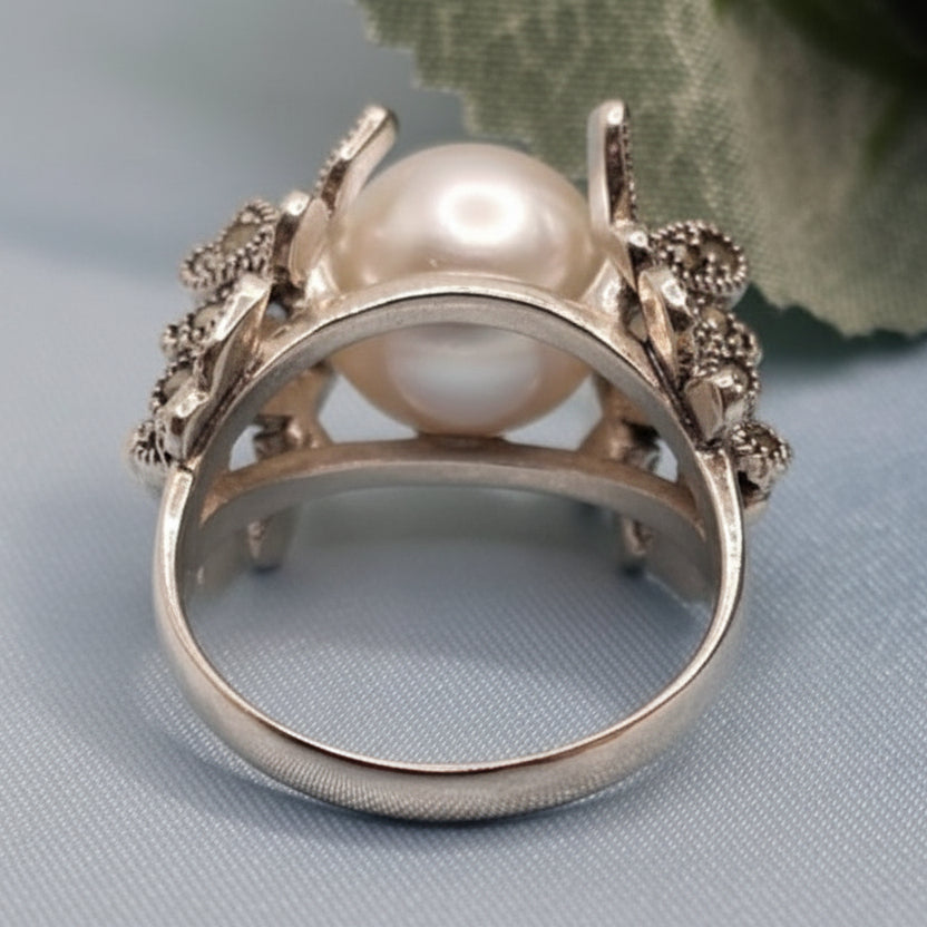 Close-up of a silver ring with a pearl on a light blue fabric background