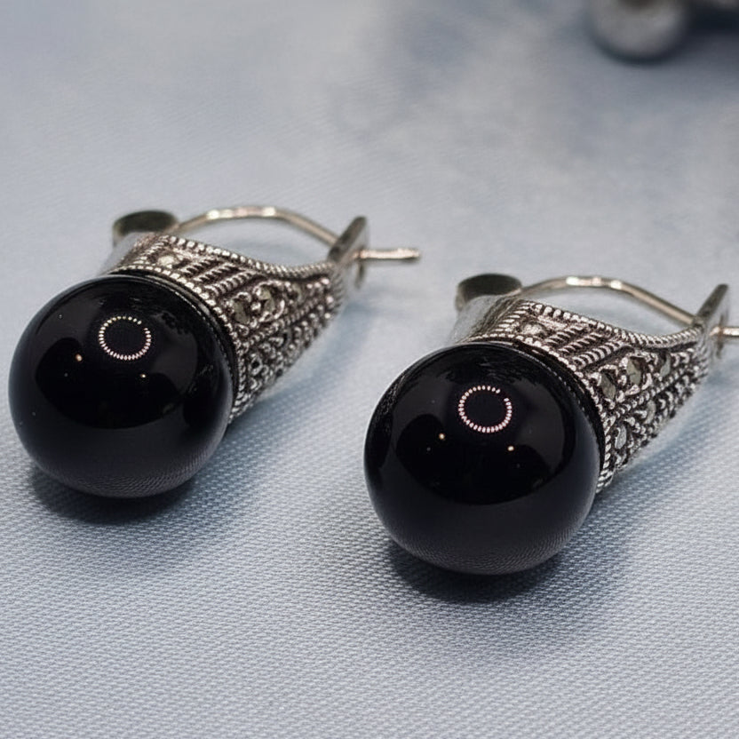 Pair of black earrings with silver hooks on a light blue fabric background