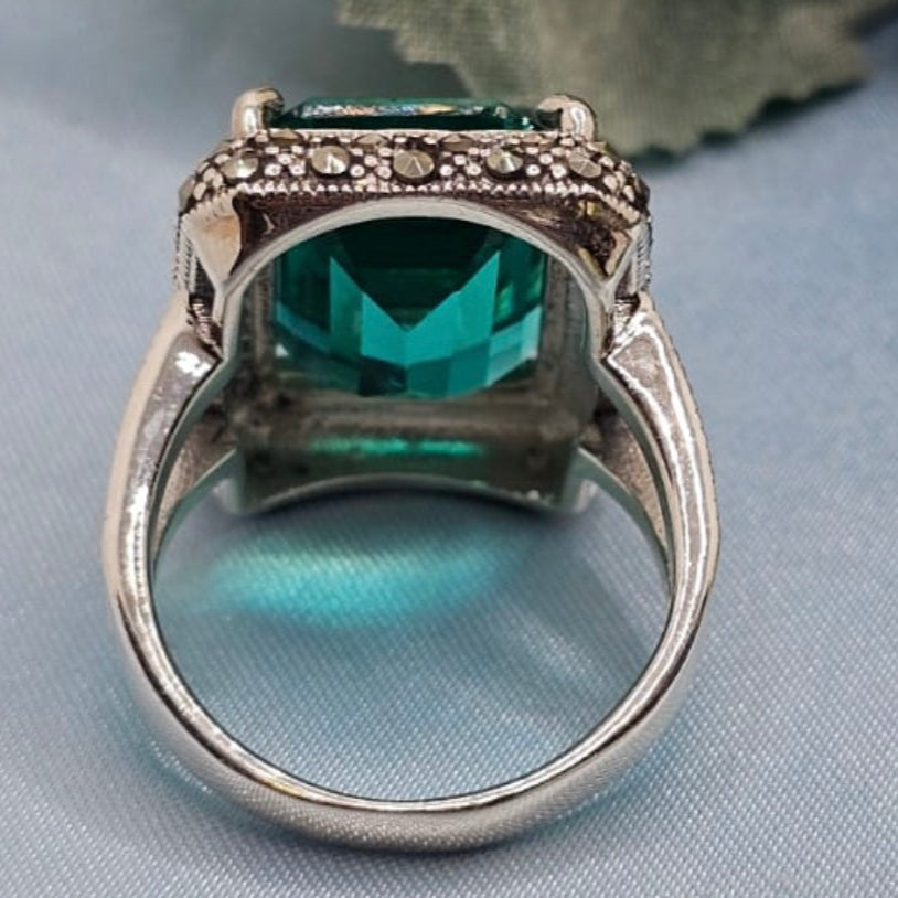 Silver ring with a green gemstone on a light blue fabric background