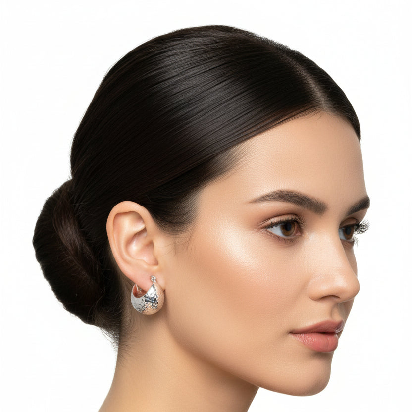 Pair of silver hoop earrings with star-like patterns on a light blue fabric background