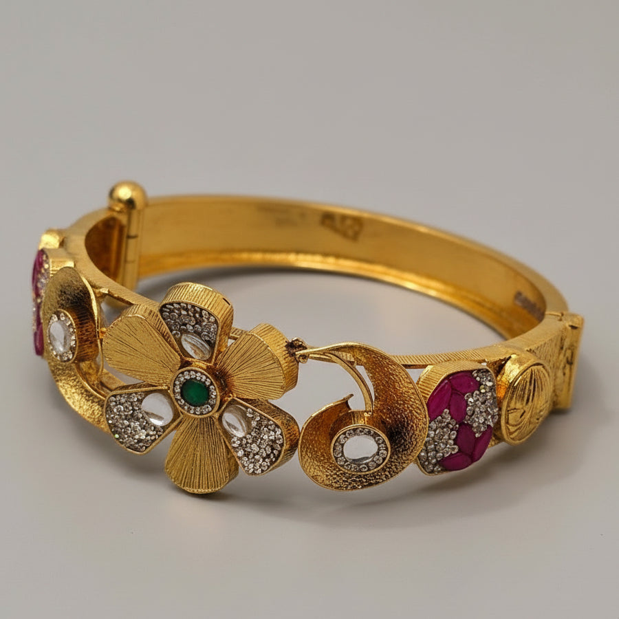 Gold bracelet with floral designs and gemstones on a light blue fabric background