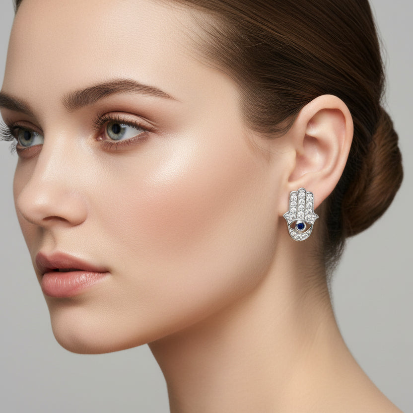 Silver Hamsa hand earrings with blue stone on a finger
