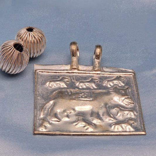 Silver pendant with a bear design on a blue fabric background