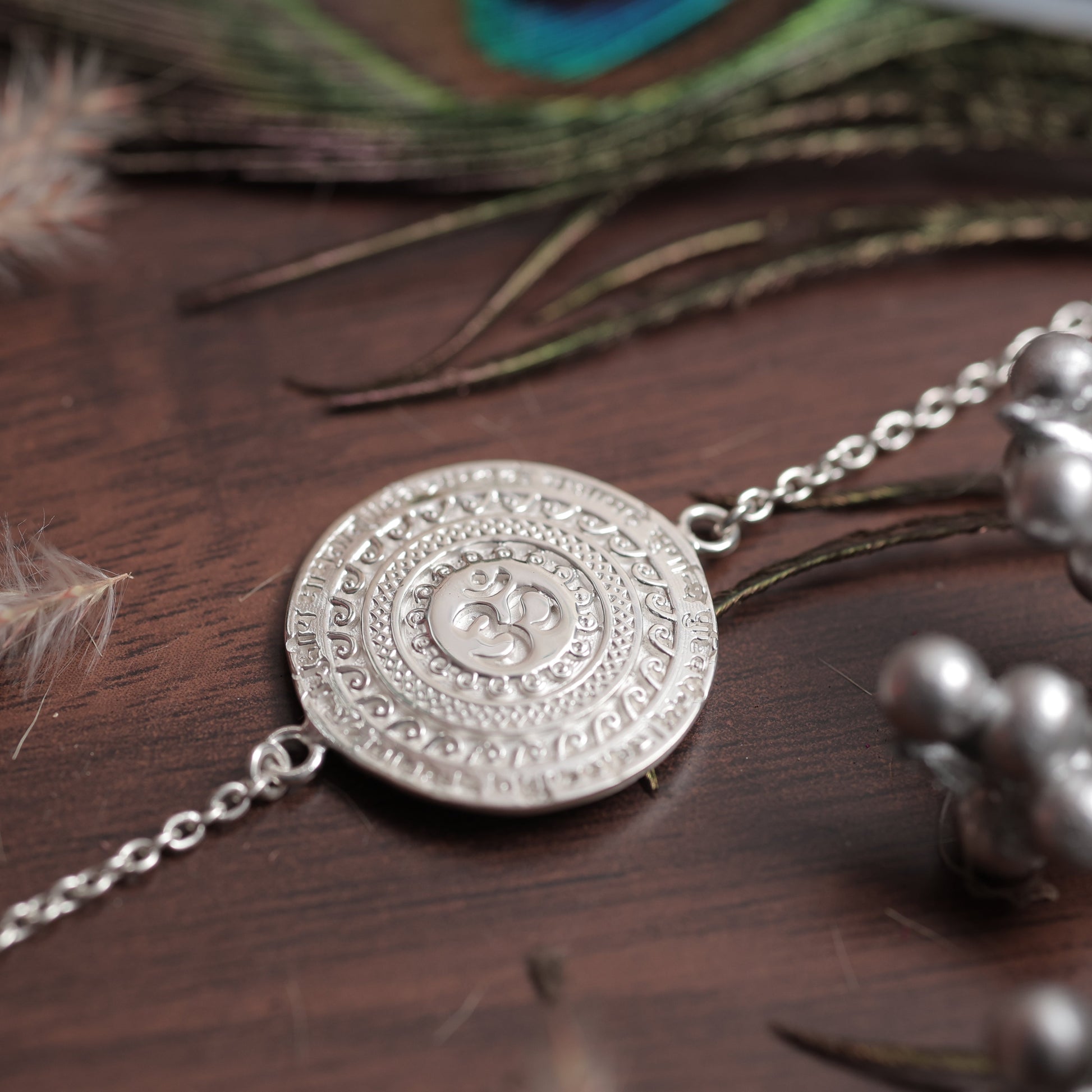 Silver necklace with decorative pendant on a wooden surface with feathers and flowers.