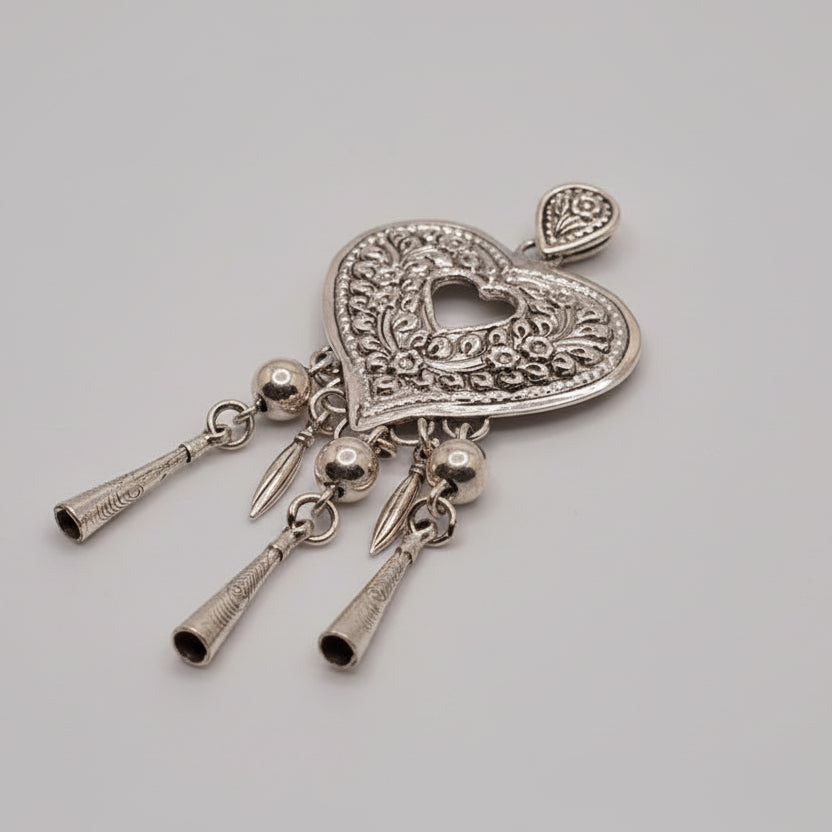 Decorative silver heart-shaped pendant with hanging elements on a light blue fabric background