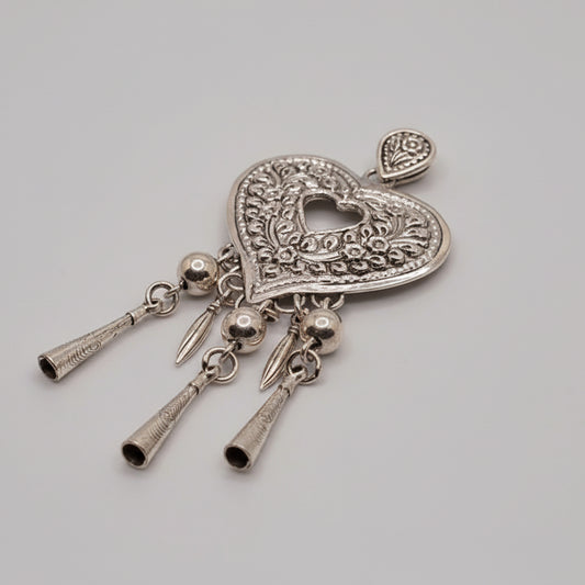 Decorative silver heart-shaped pendant with hanging elements on a light blue fabric background