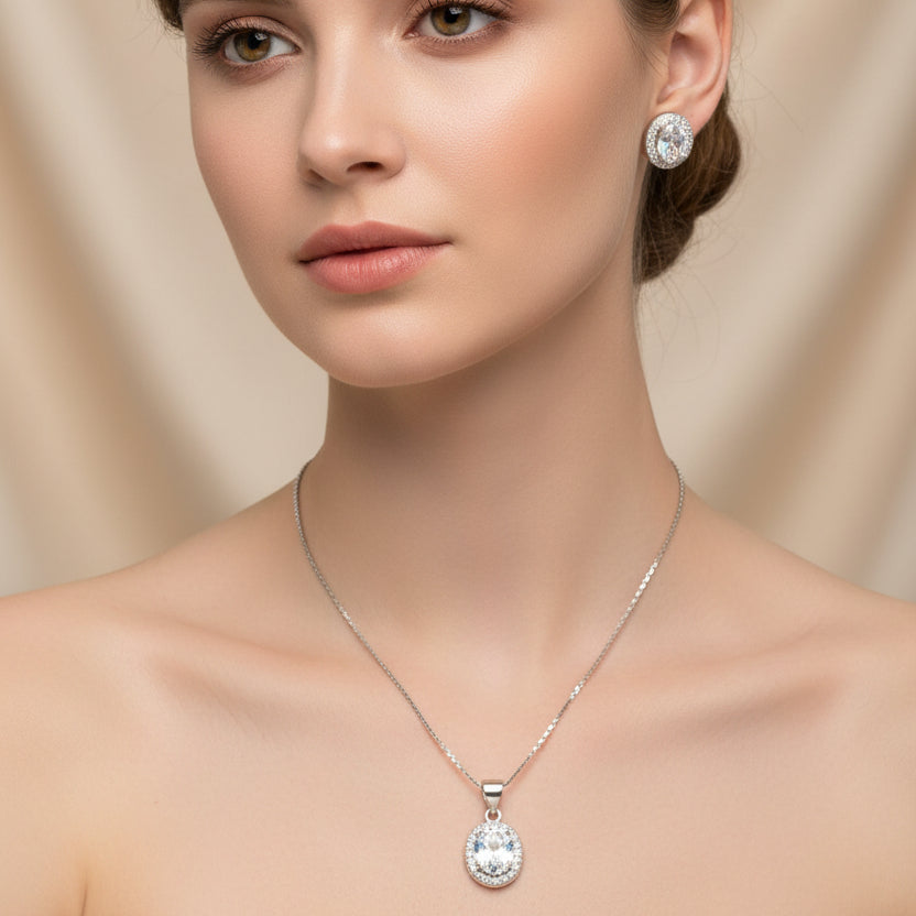 Silver jewelry set with pendant and earrings on a light gray surface.