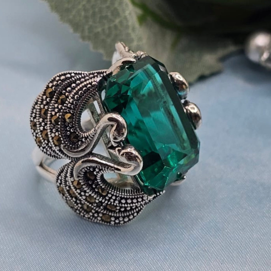Silver ring with a large green gemstone on a light blue fabric background