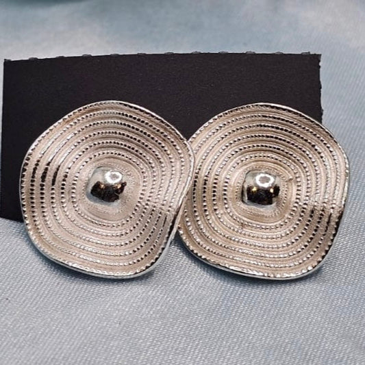 Pair of silver circular earrings on a black cushion against a gray background