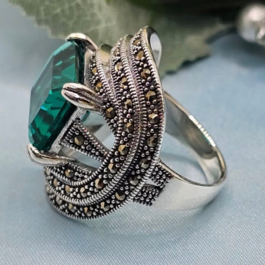 Silver ring with green gemstone on a light blue fabric background