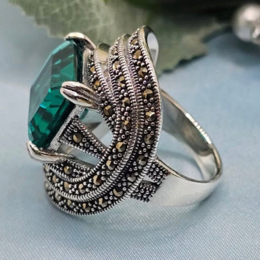 Silver ring with green gemstone on a light blue fabric background