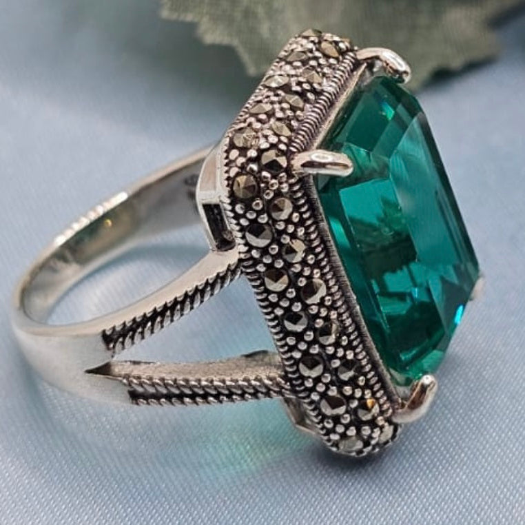 Silver ring with a green gemstone on a light blue background