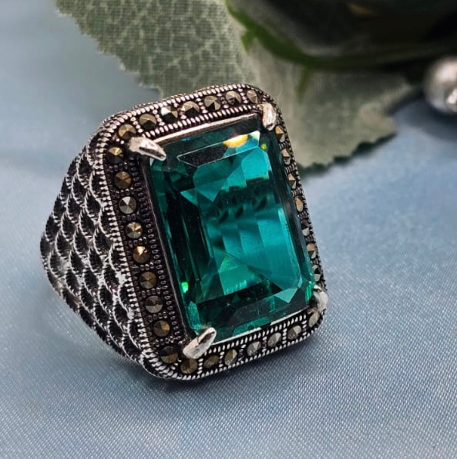 Ring with a large green gemstone and intricate metalwork on a light blue fabric background