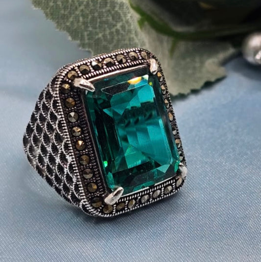 Ring with a large green gemstone and intricate metalwork on a light blue fabric background