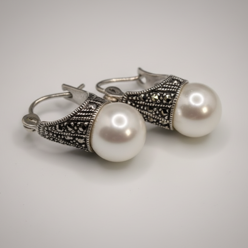 Pair of pearl earrings with silver and black decorative elements on a light gray background