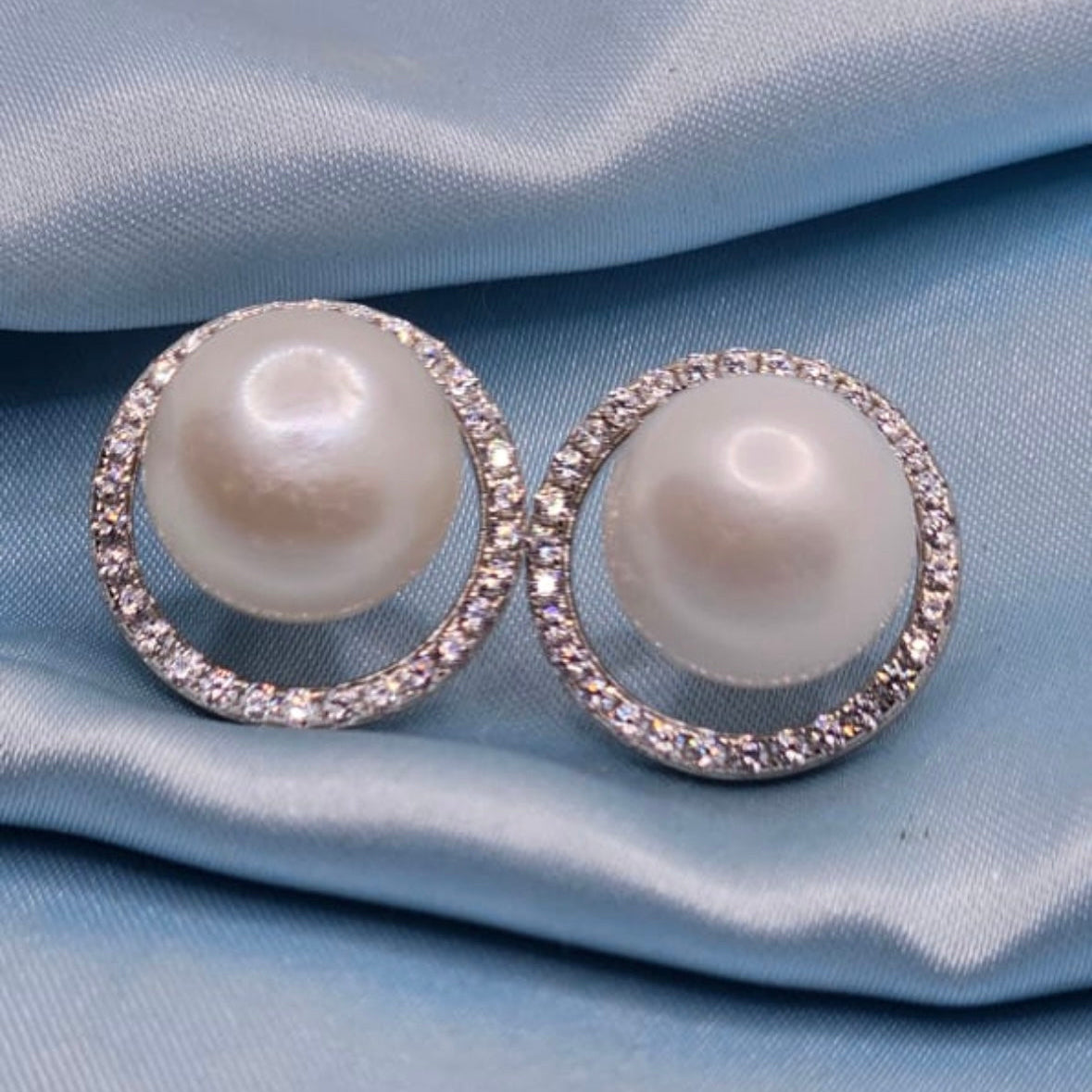 Pearl earrings with diamond accents on a light blue fabric background