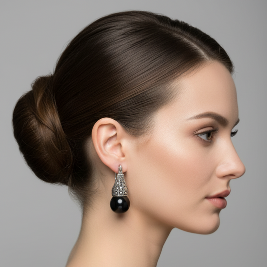 Pair of black earrings with silver hooks on a light blue fabric background