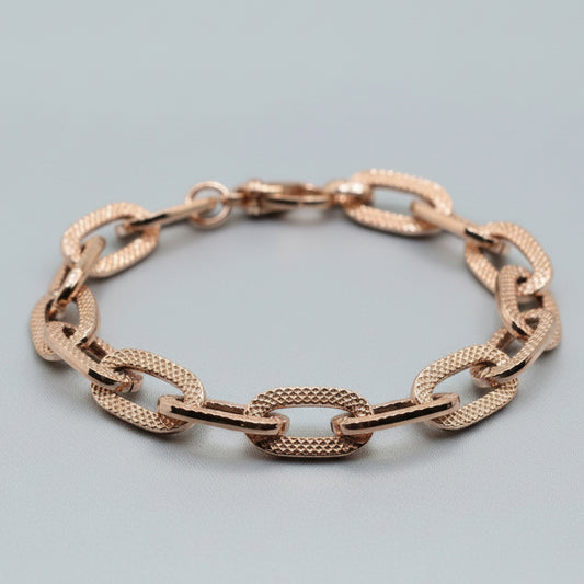 Rose gold chain bracelet on a light blue fabric background
