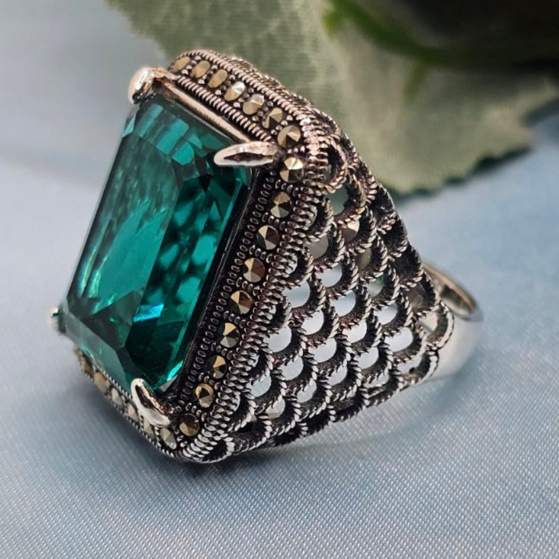 Silver ring with a large green gemstone on a light blue fabric background