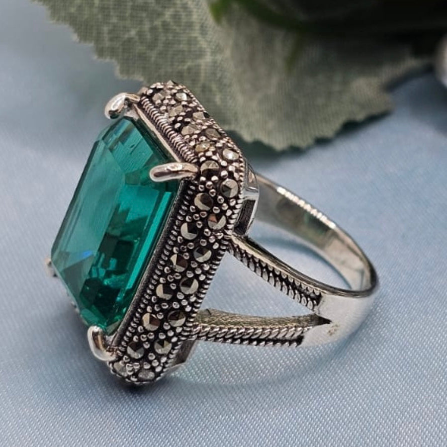 Silver ring with a large green gemstone on a light blue fabric background
