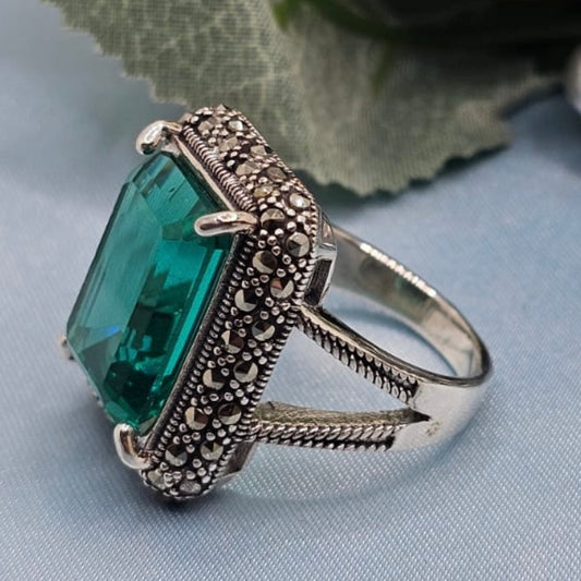 Silver ring with a large green gemstone on a light blue fabric background