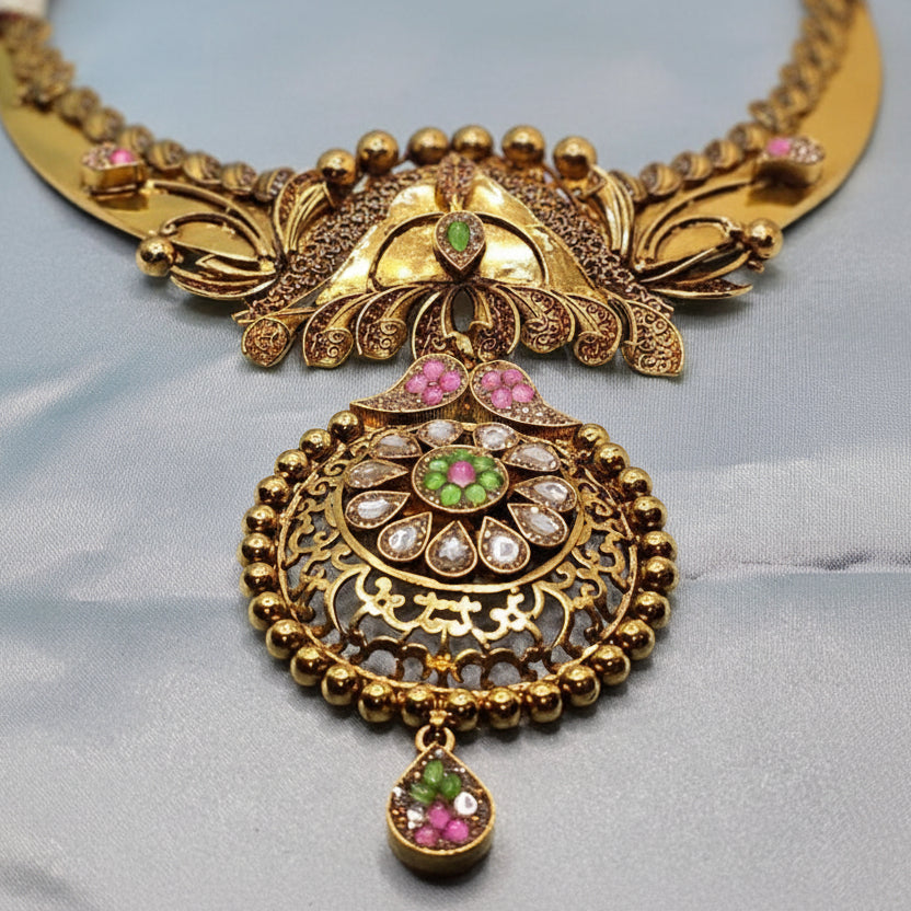 Gold necklace with intricate design and gemstones on a light gray background