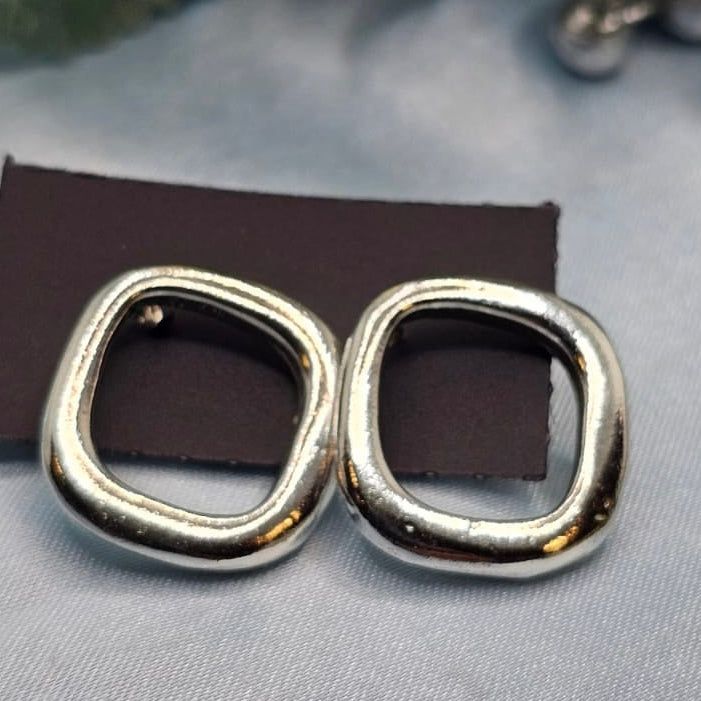 Pair of silver hoop earrings on a gray surface with a brown card underneath.