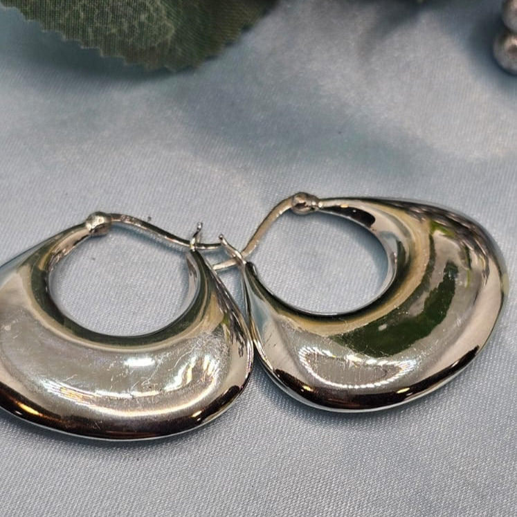 Silver hoop earrings on a gray surface with green leaves in the background