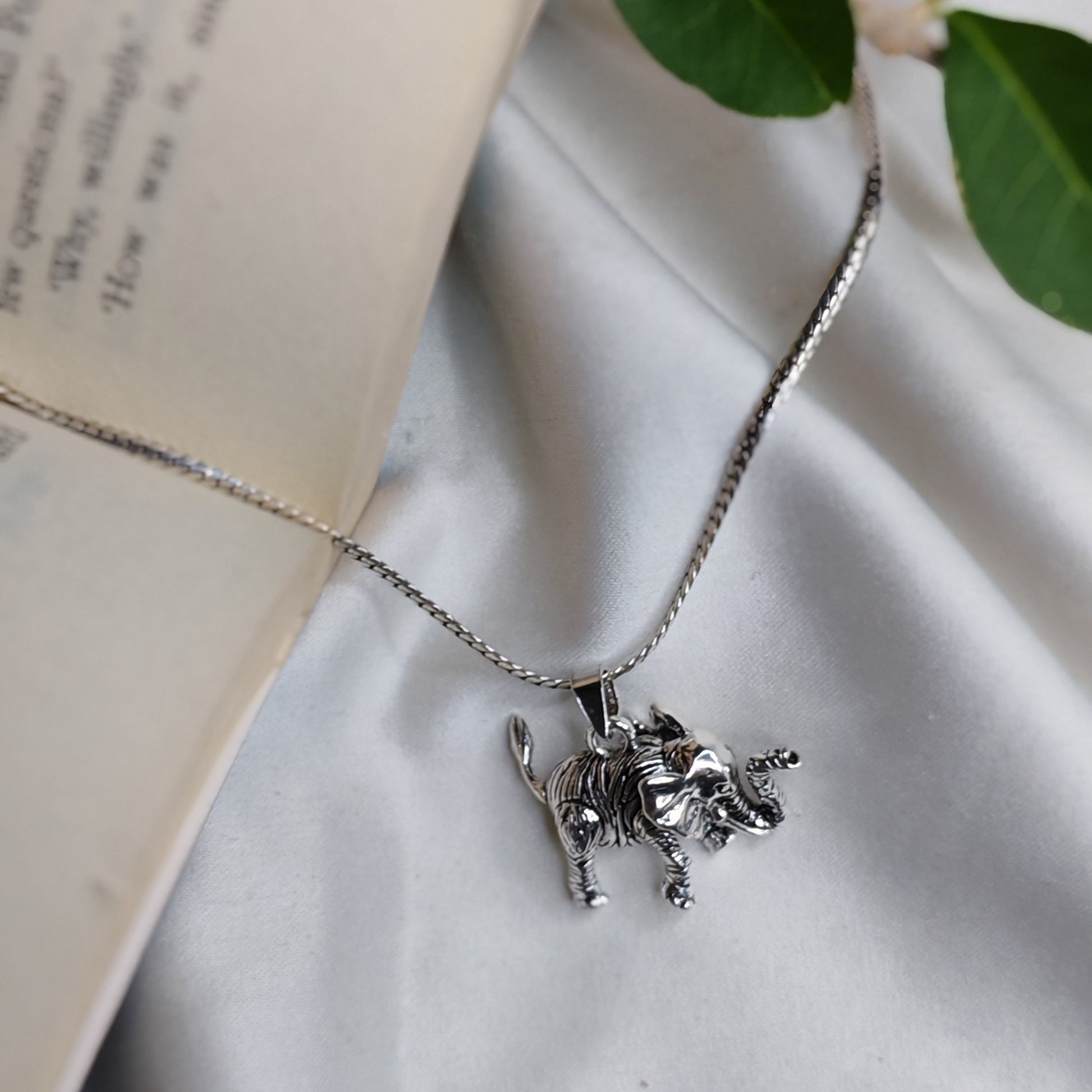 Silver necklace with a pendant on a white surface next to an open book